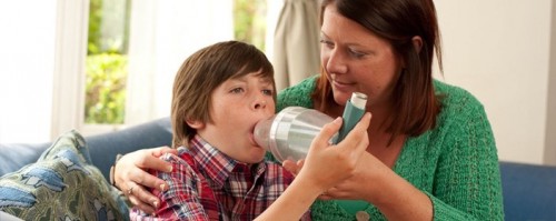boy being helped use a nebulizer by his mother during an asthma attack