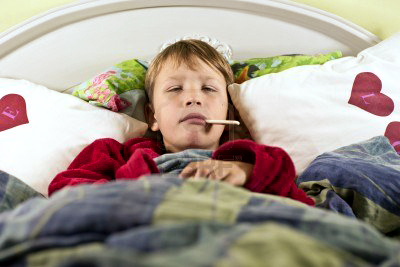 Boy in bed with flu and thermometer in his mouth
