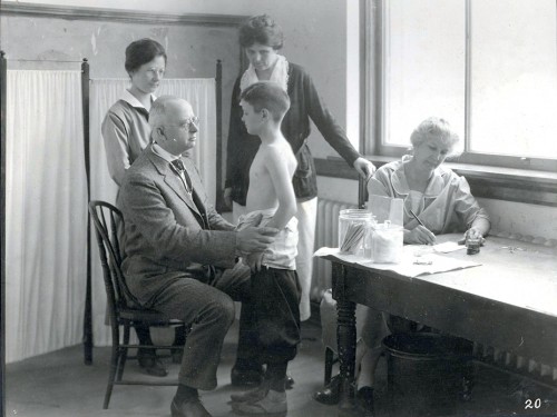 Vintage photograph of a school boy receiving a physical exam from the school doctor.