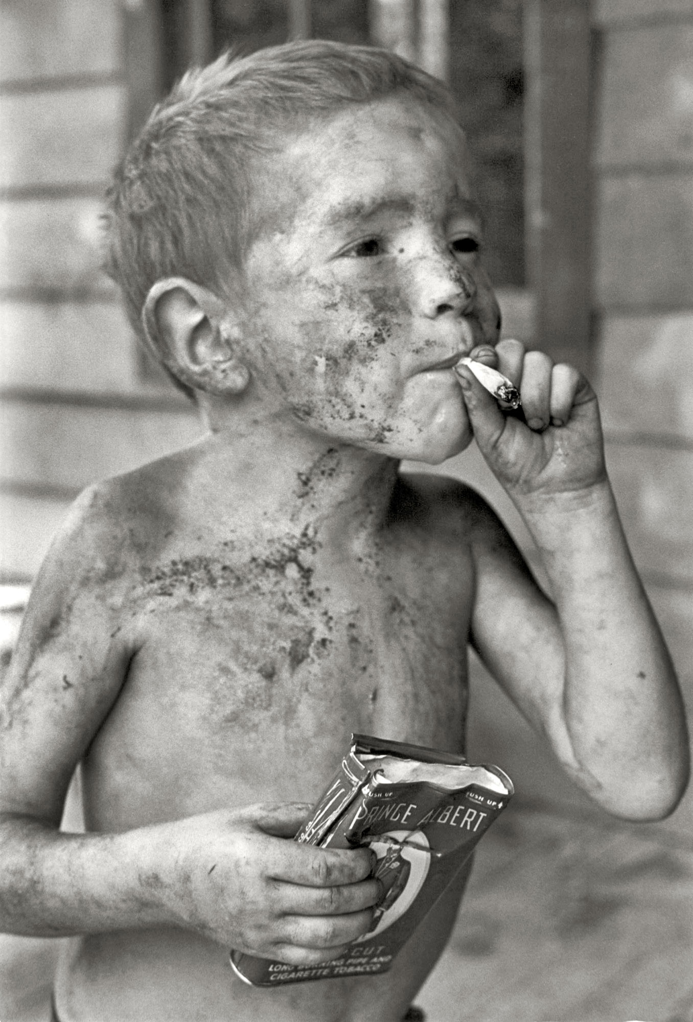 Unkempt child holding his tobacco pack and smoking a cigarette.