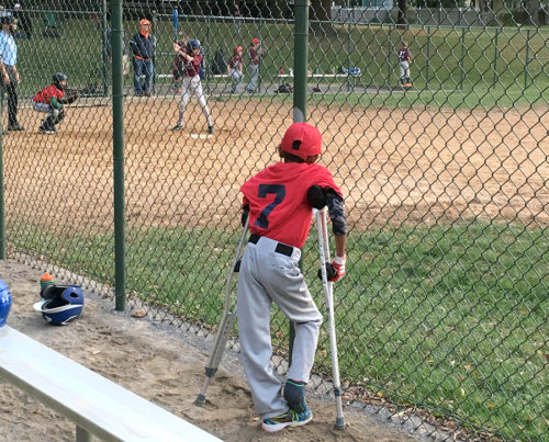 Boy in cast and crutches looks onto baseball field
